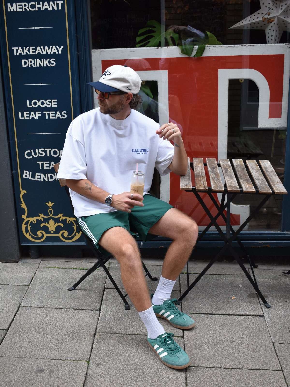 Man wearing white t-shirt, green athletic shorts, and green sneakers at a cafe.