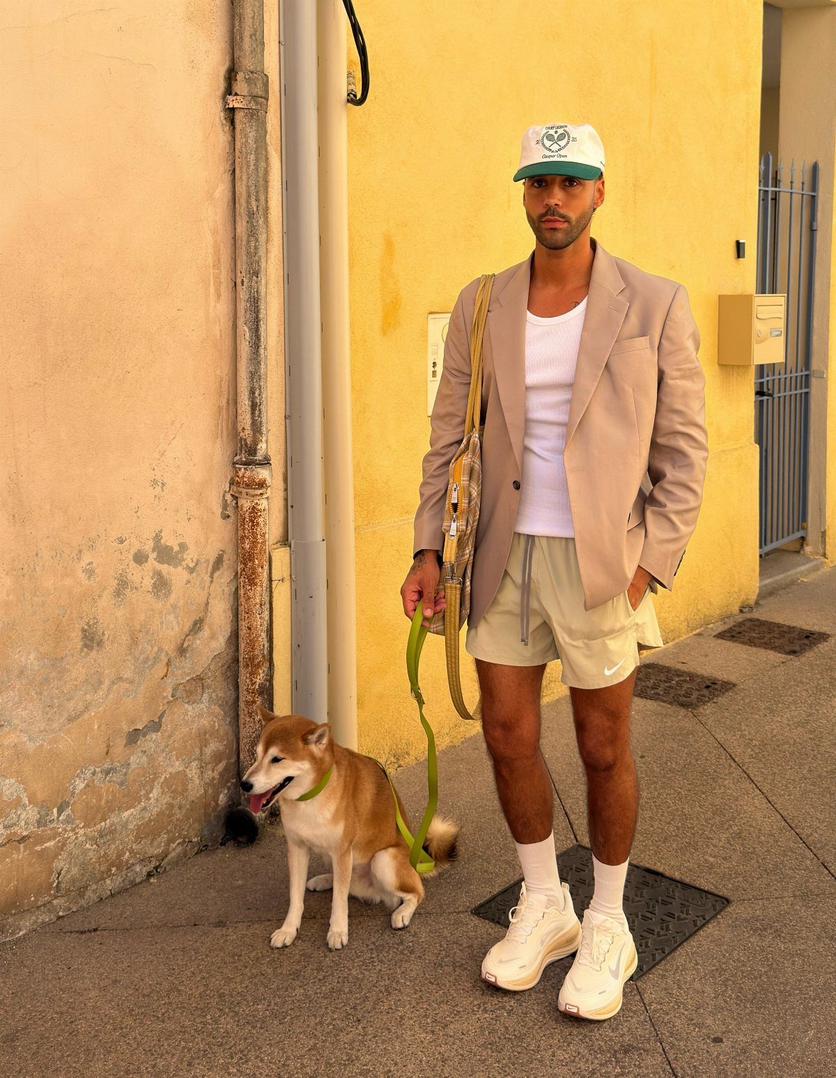 Man in tan blazer and athletic shorts standing with a Shiba Inu dog.