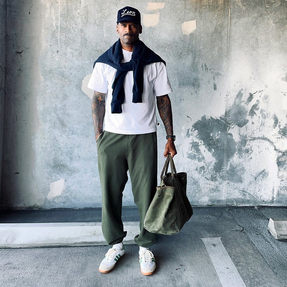 Man in white t-shirt, olive trousers, and navy sweater draped over shoulders.