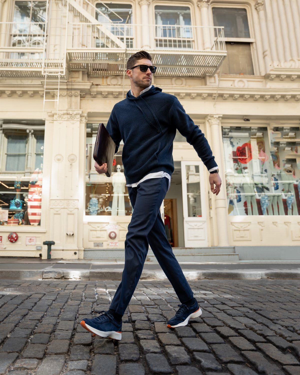 Man in navy hoodie and matching trousers walking on a cobblestone city street