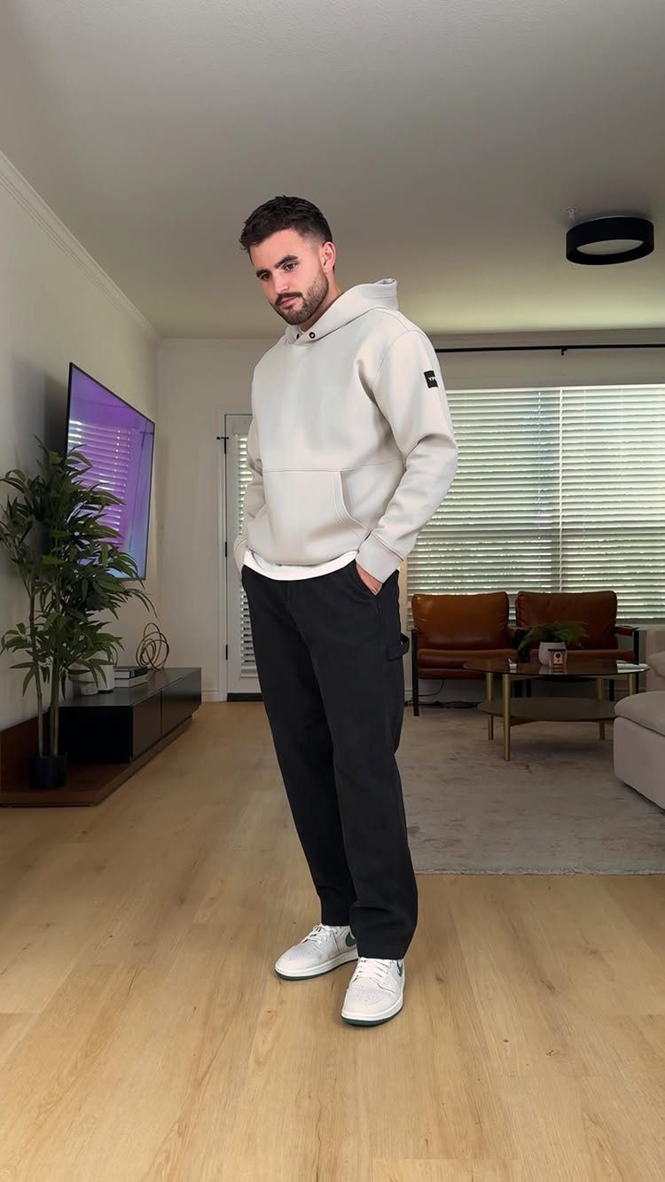 Man wearing a beige oversized hoodie, black sporty pants, and white sneakers.