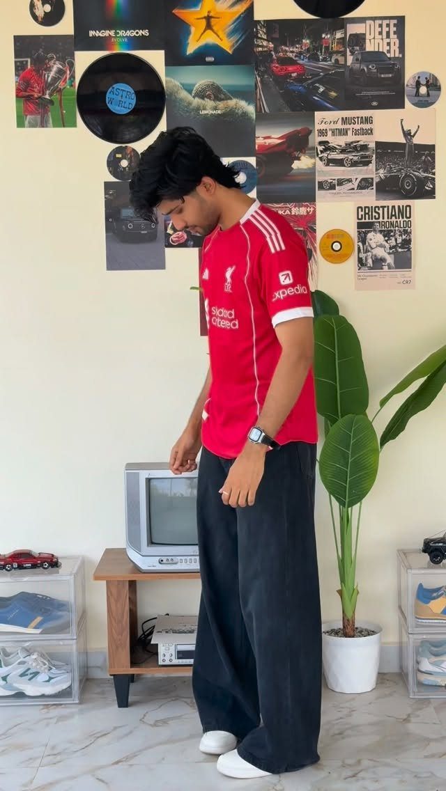 Man wearing a red sports jersey and wide black trousers in a decorated room