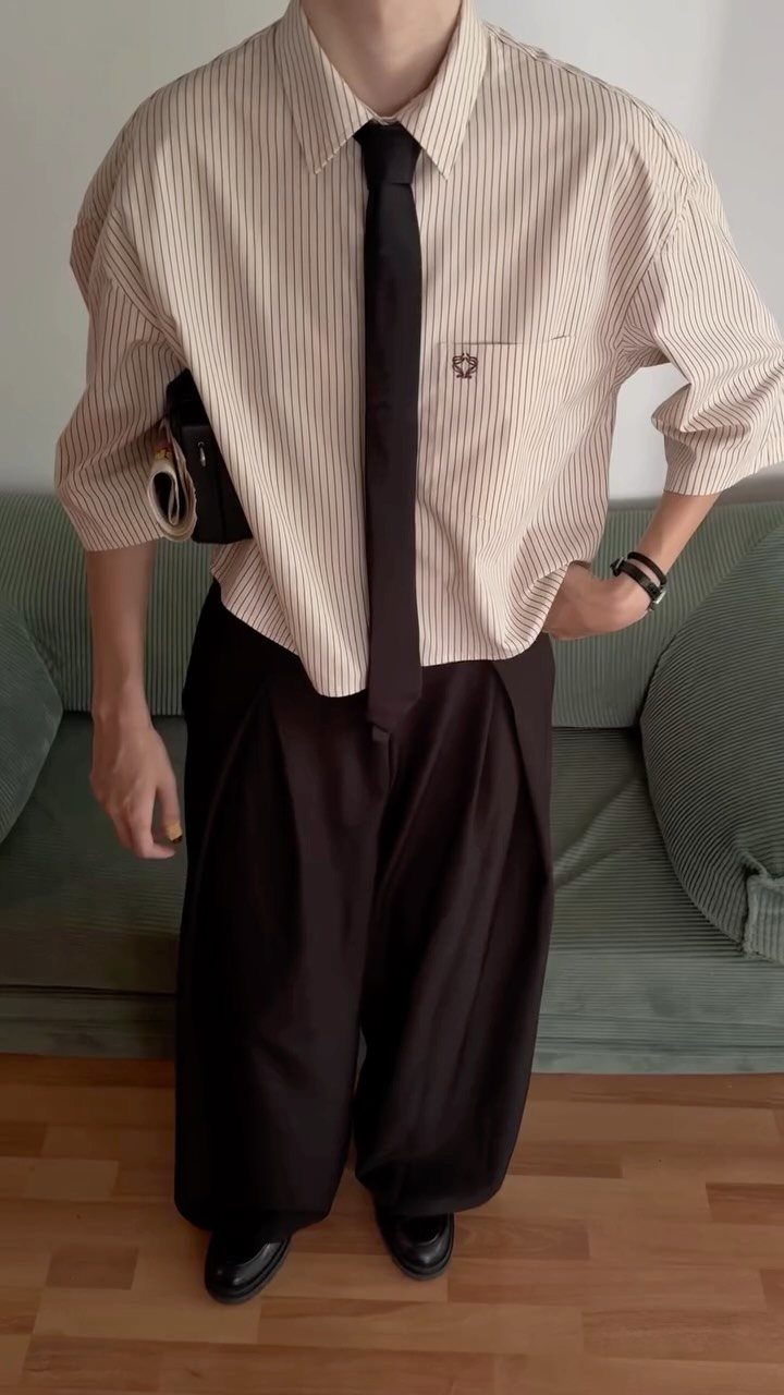 Person wearing a striped shirt, black tie, and wide-leg black tailored trousers.