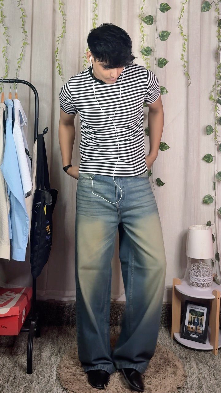 Man wearing a striped t-shirt and wide-leg blue jeans standing in a room.