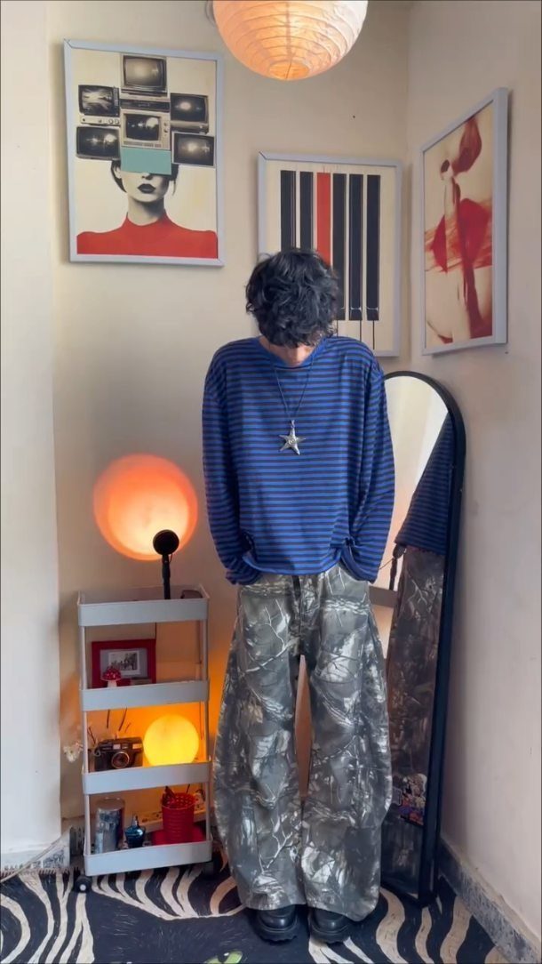 Person from behind wearing a blue striped shirt and camouflage wide-leg trousers.