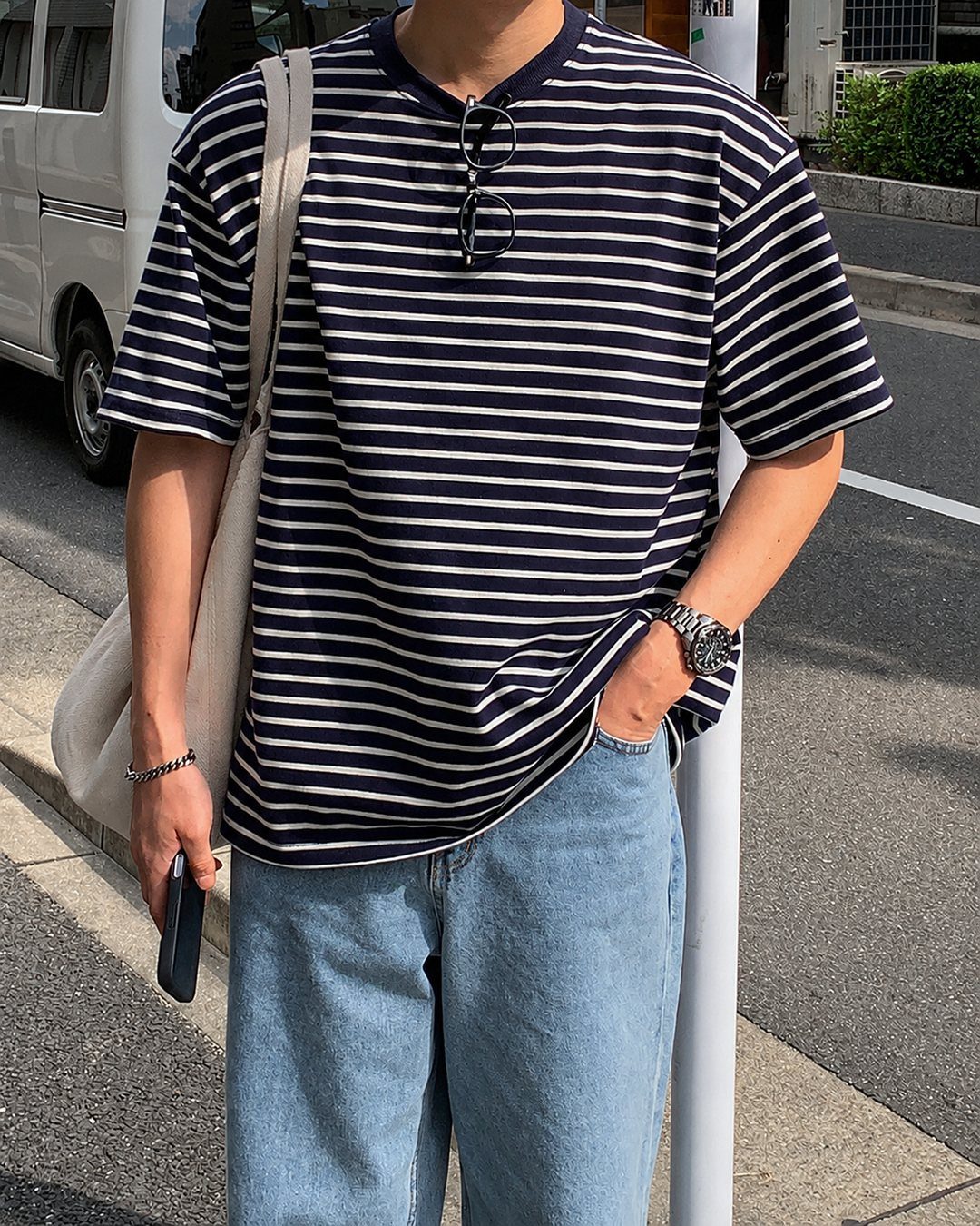 Person wearing a navy striped t-shirt, light blue jeans, and a white bag.