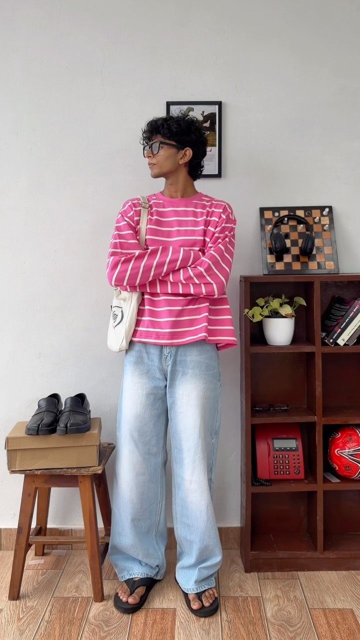Person wearing pink horizontal striped shirt and light blue wide-leg jeans standing indoors.