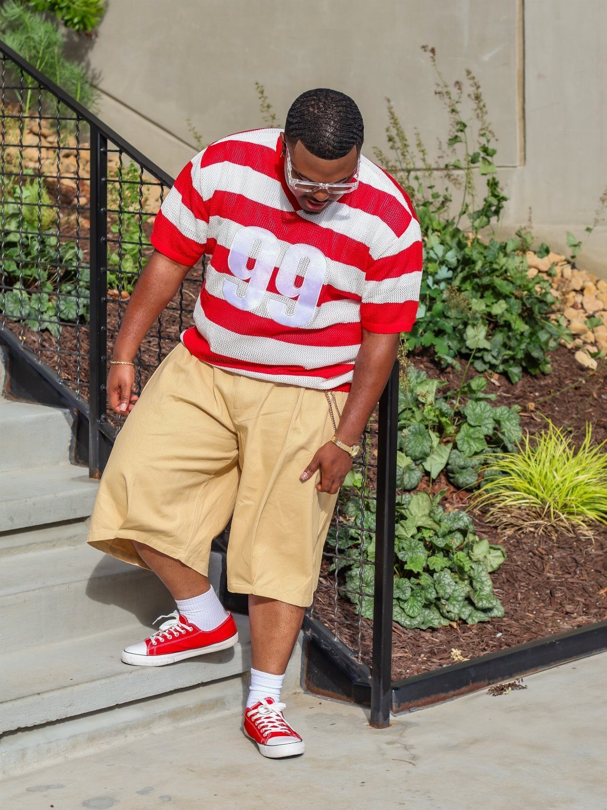 Man in red and white striped t-shirt and tan shorts standing outdoors.