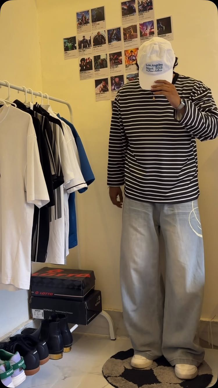 Person wearing a striped long-sleeve t-shirt, baggy grey pants, and a white cap.