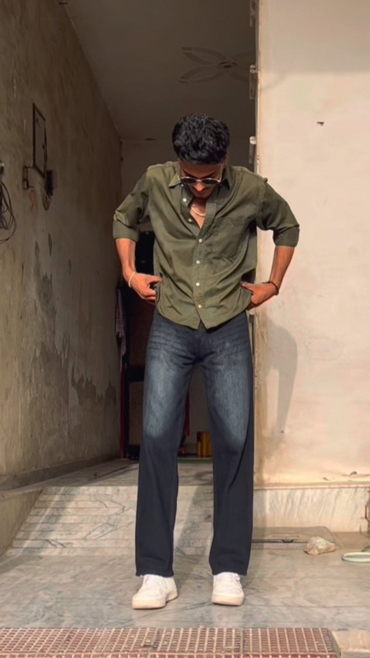 Man wearing olive green shirt and dark blue straight leg jeans with white sneakers