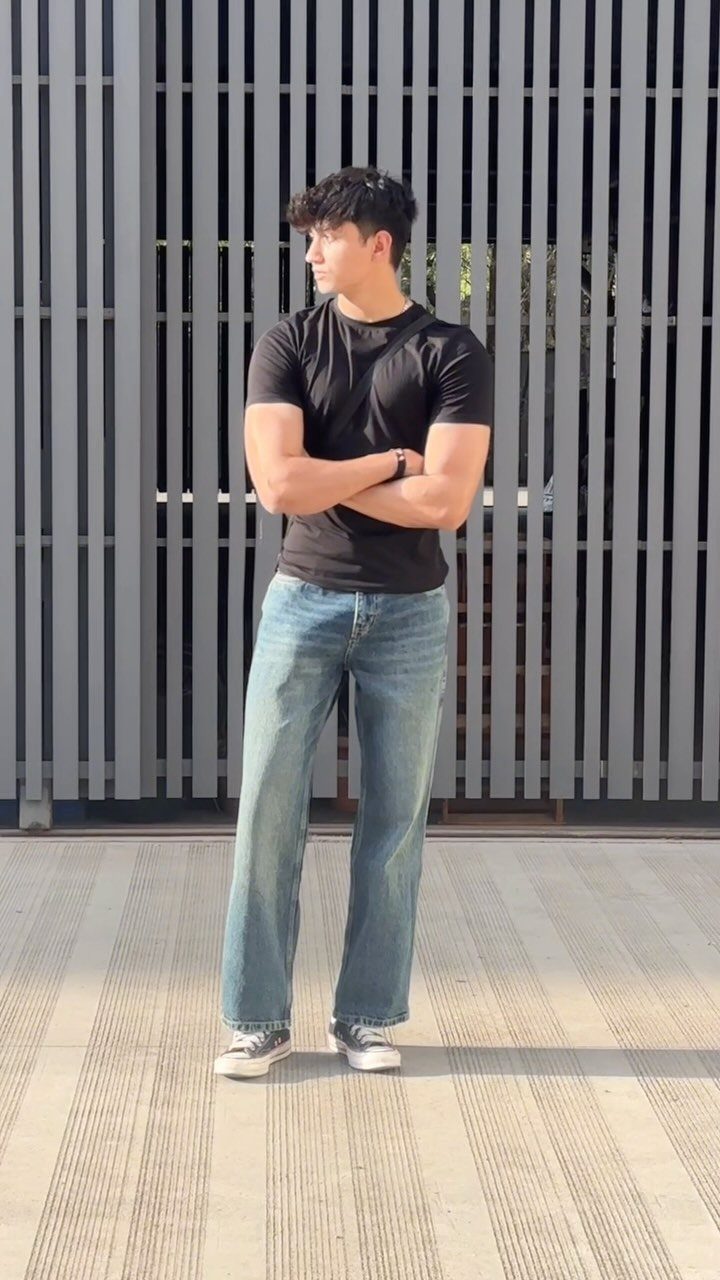 Muscular man wearing a black t-shirt and light-wash straight-leg jeans standing outdoors.