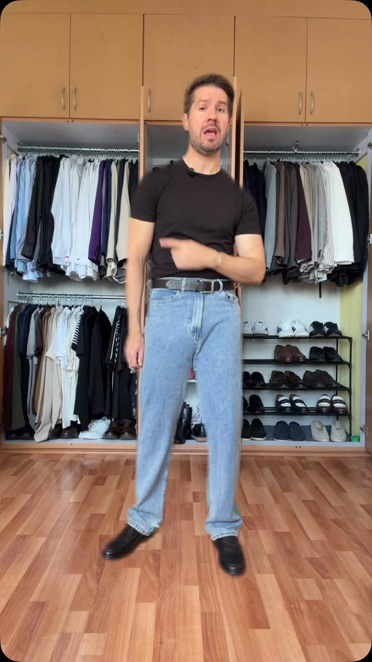 Man wearing light blue straight leg jeans and black t-shirt in a closet