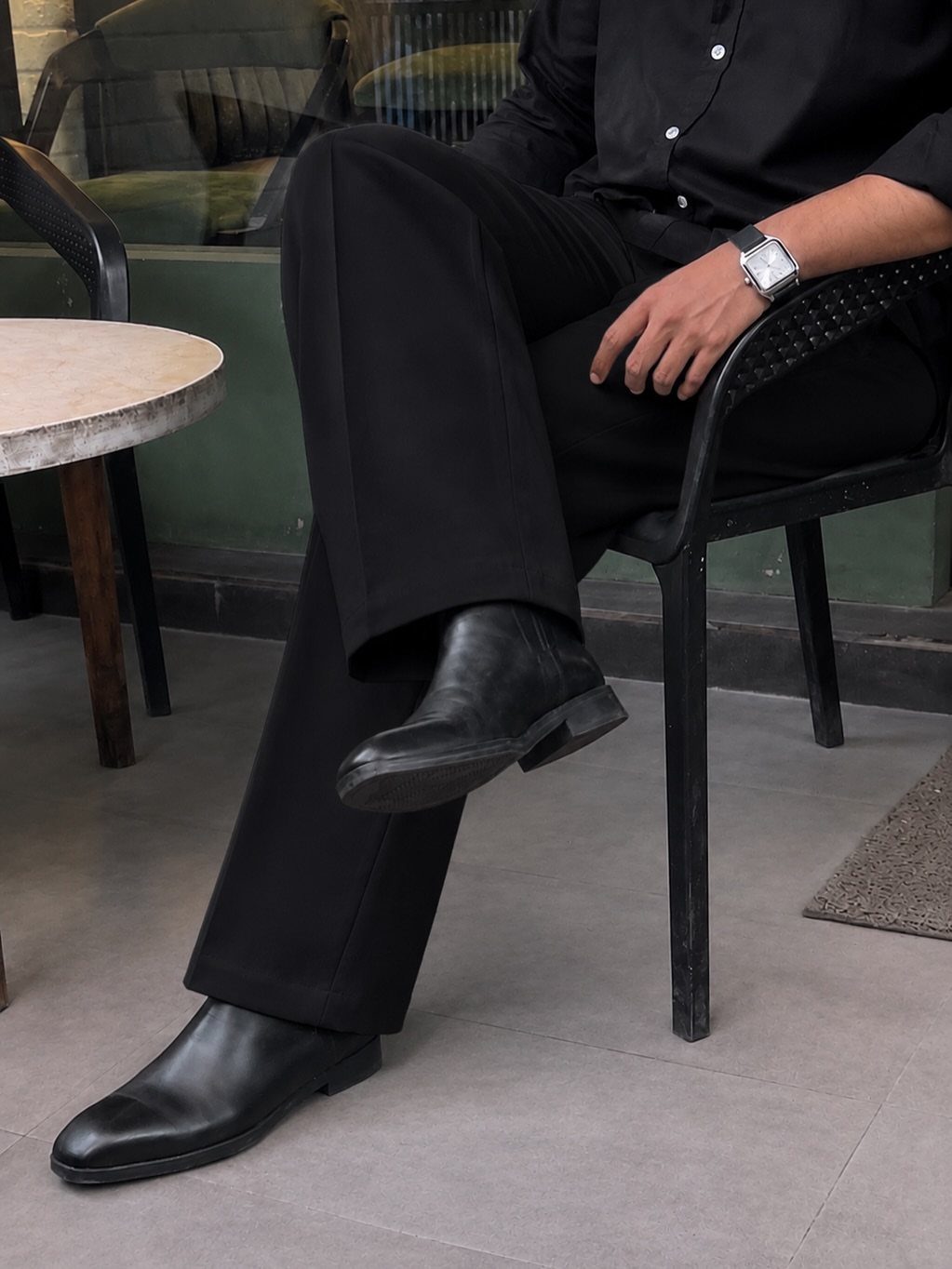 Person wearing black wide-leg trousers and leather boots sitting in a black chair.