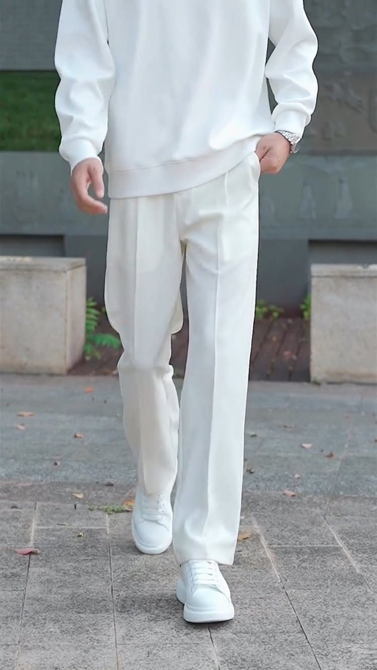 Person wearing white pleated wide-leg trousers and a white long-sleeved shirt with sneakers.
