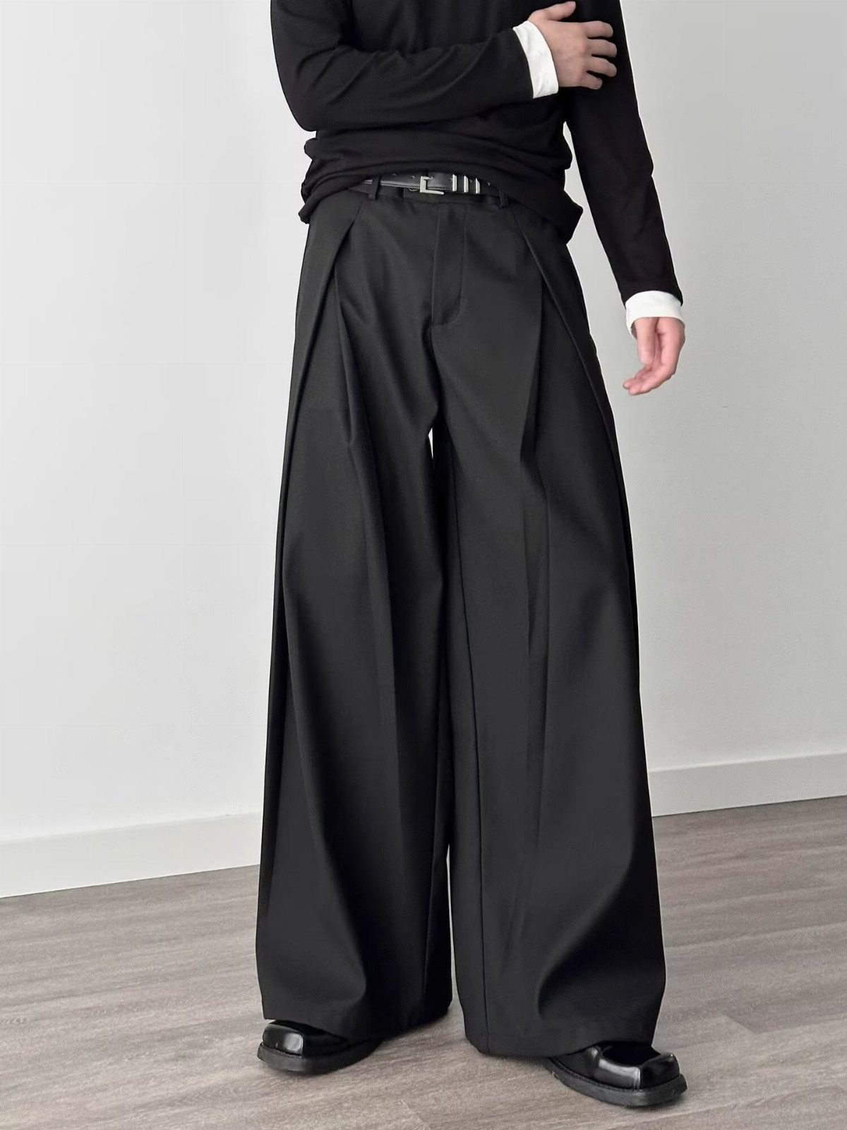 Person wearing pleated black wide-leg trousers and a black long-sleeved shirt.