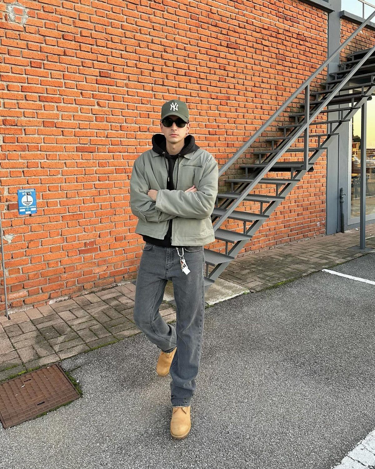 Man wearing a light green chore jacket and grey wide-leg jeans standing outdoors.