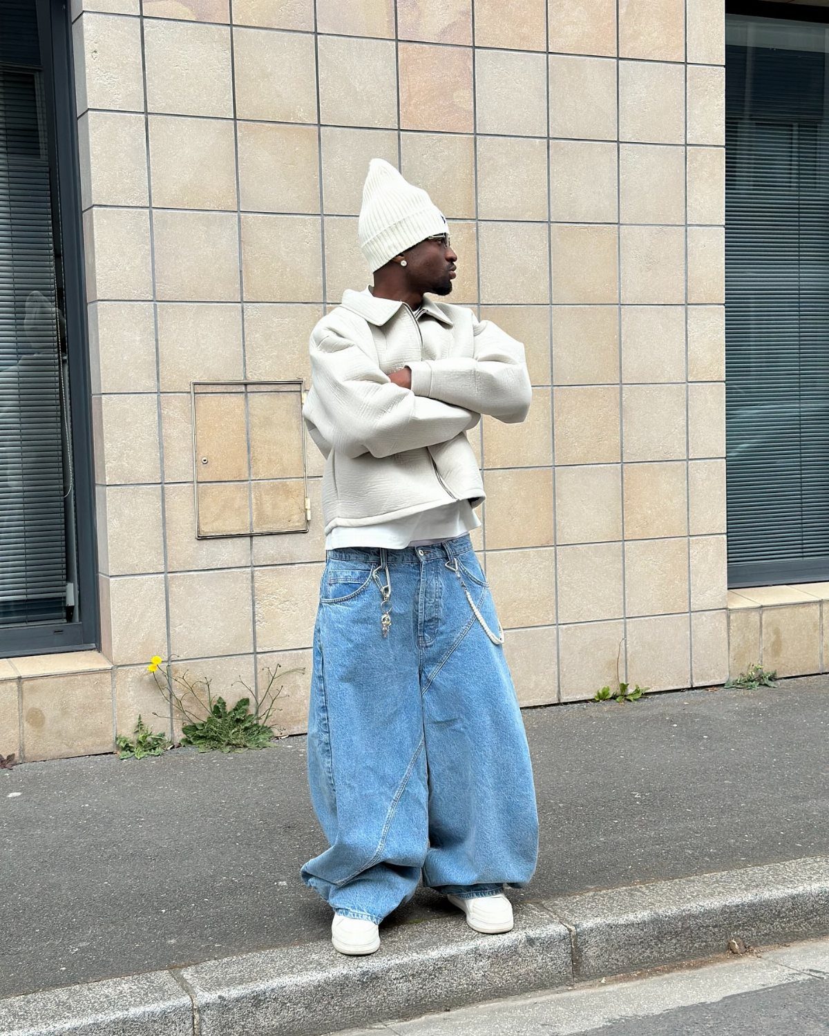 Person in white cropped jacket and oversized wide-leg blue jeans standing by tiled wall