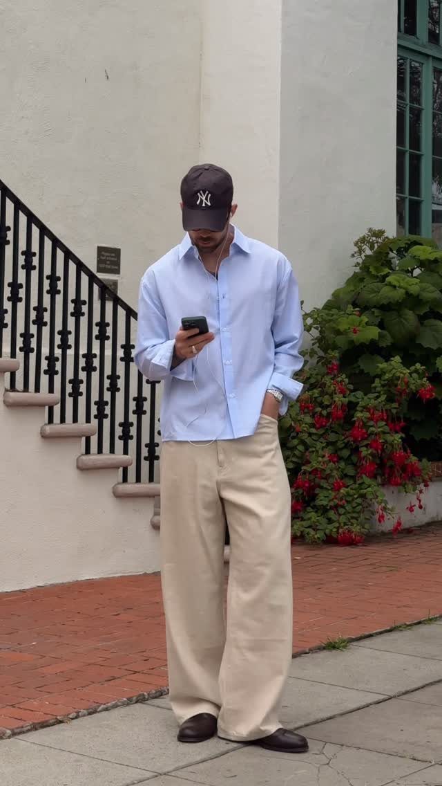 Man in light blue shirt and beige wide-leg trousers wearing dark dress shoes.