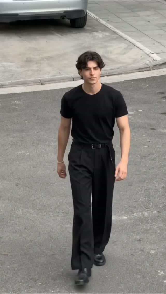 Man wearing a fitted black t-shirt tucked into black wide-leg trousers walking outdoors.
