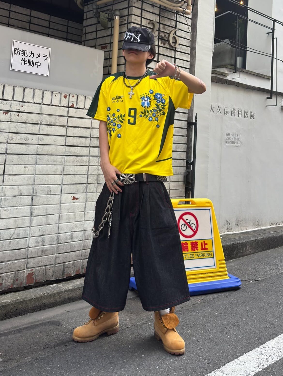 Person in yellow soccer jersey and black wide-leg pants standing on city street