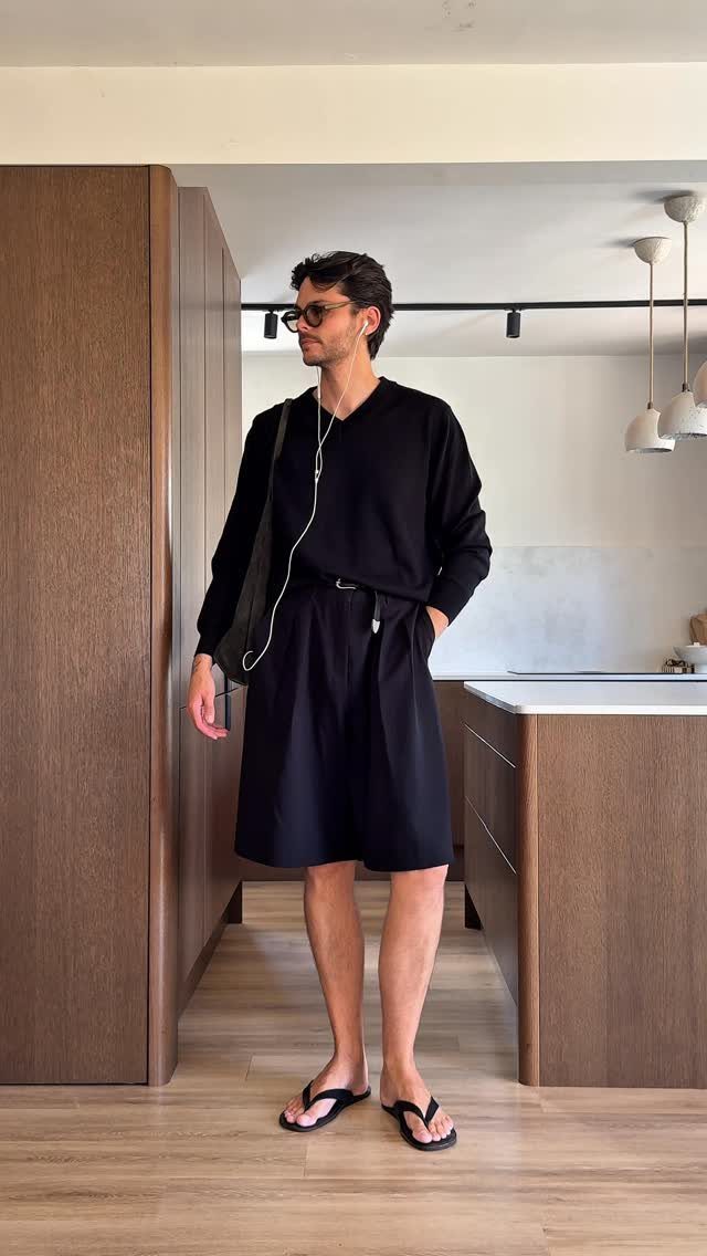 Man wearing black long-sleeved shirt and knee-length Bermuda shorts in a modern kitchen