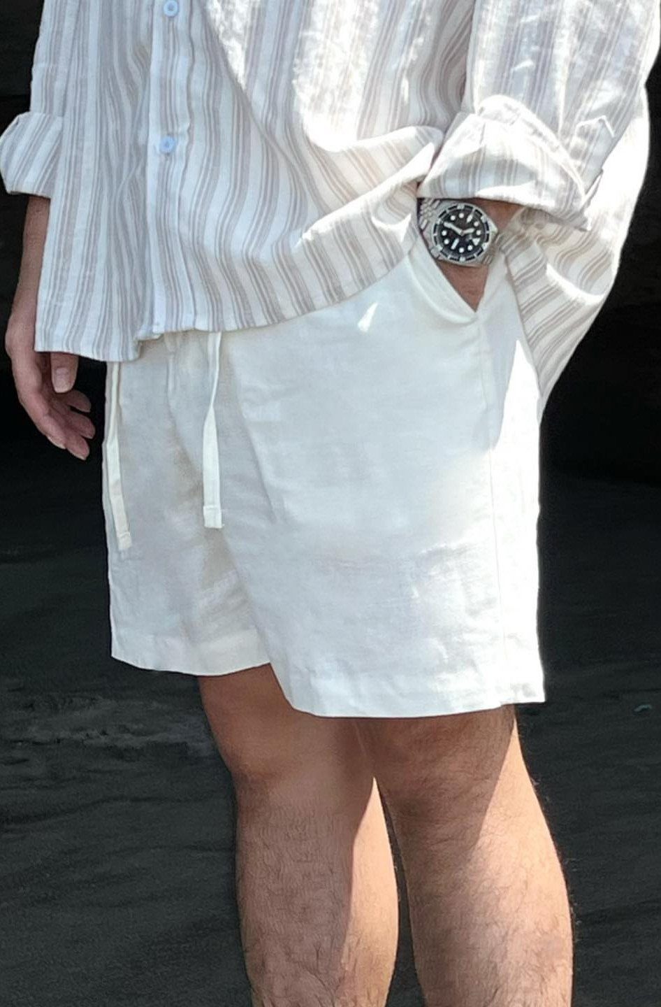 White linen drawstring shorts paired with a striped button-down shirt and silver watch.