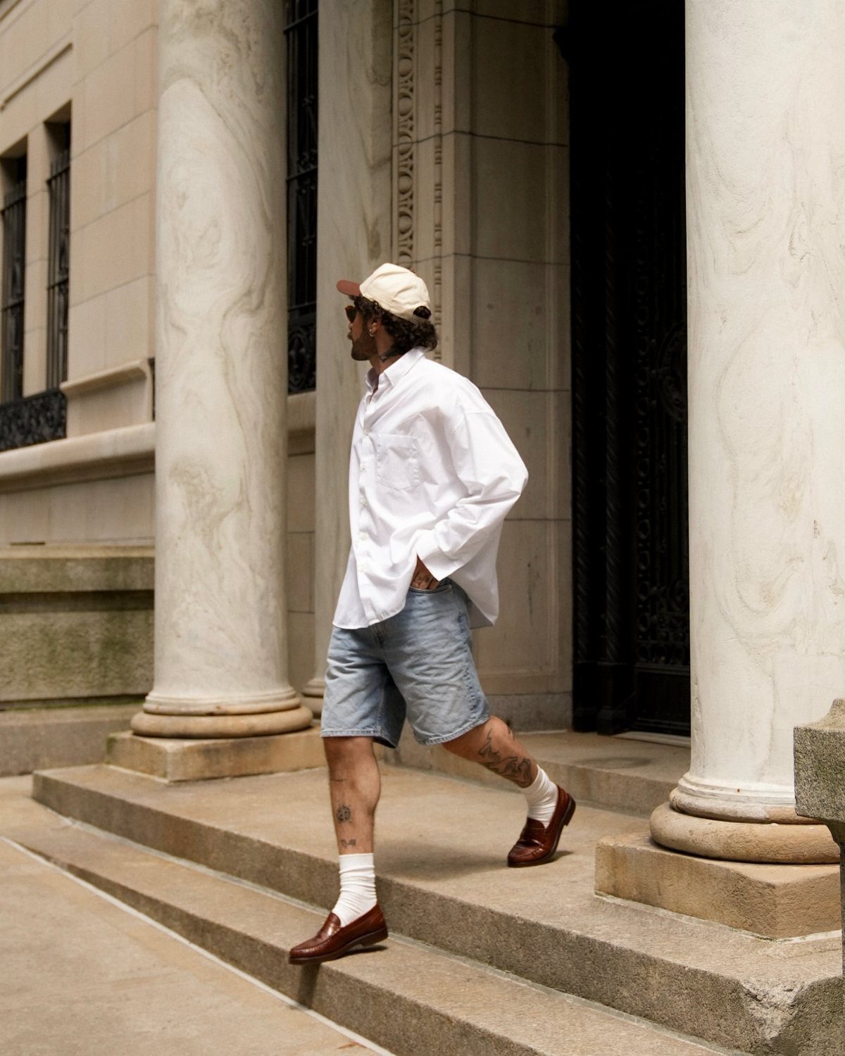Man wearing light blue shorts and brown leather loafers walking up stone steps.