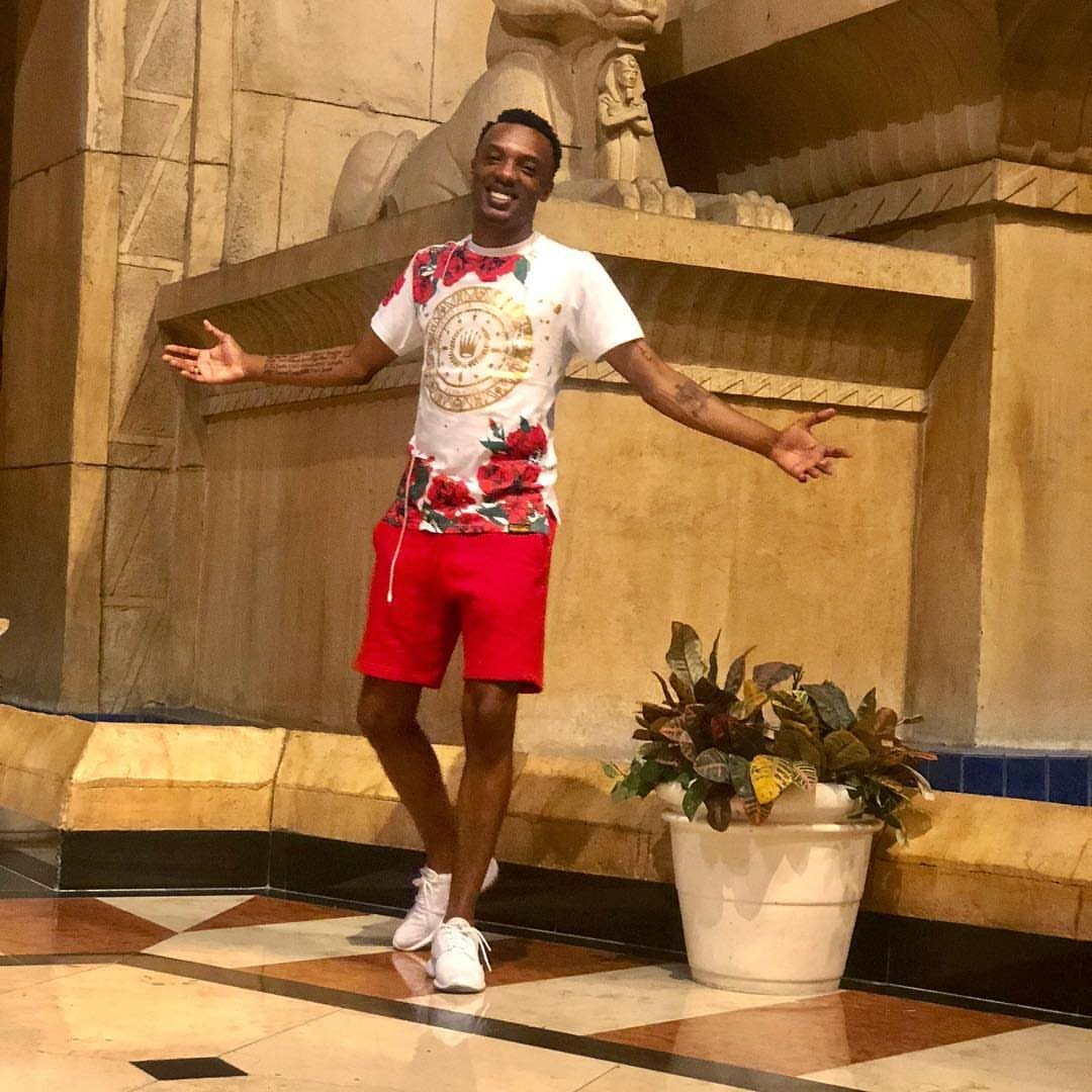 Man wearing a floral white t-shirt and red short shorts with white sneakers.