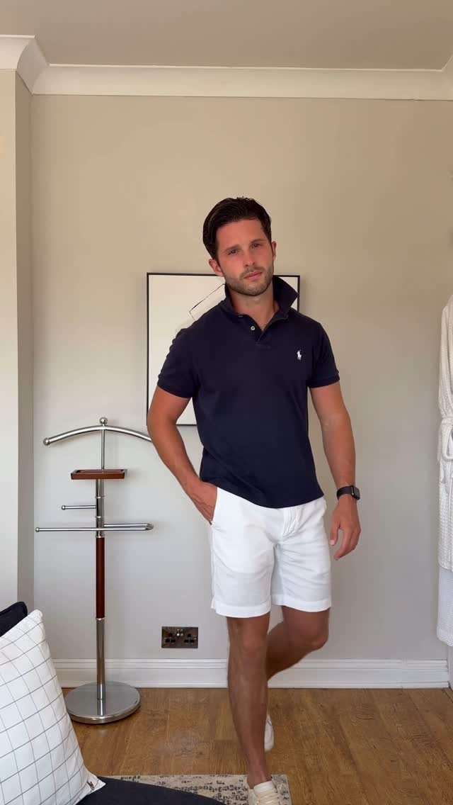 Man wearing a navy polo shirt and white shorts standing in a room.