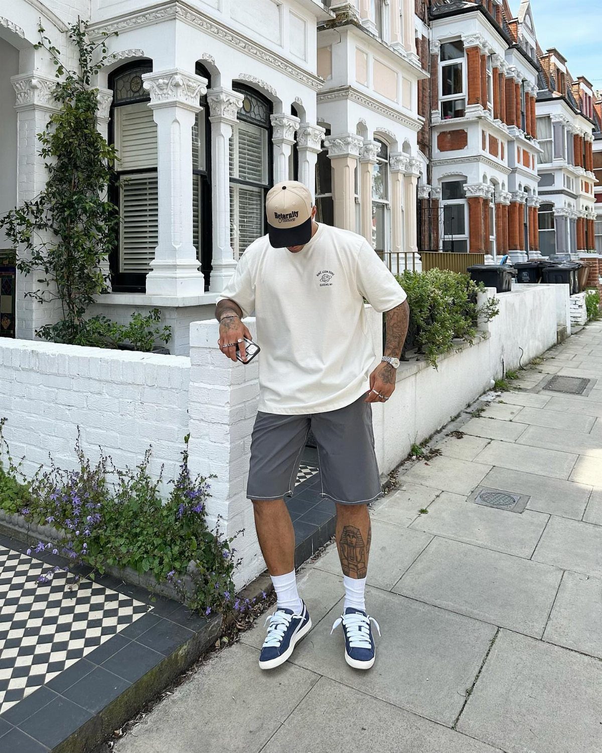 Man wearing beige t-shirt and grey shorts with blue sneakers on city sidewalk