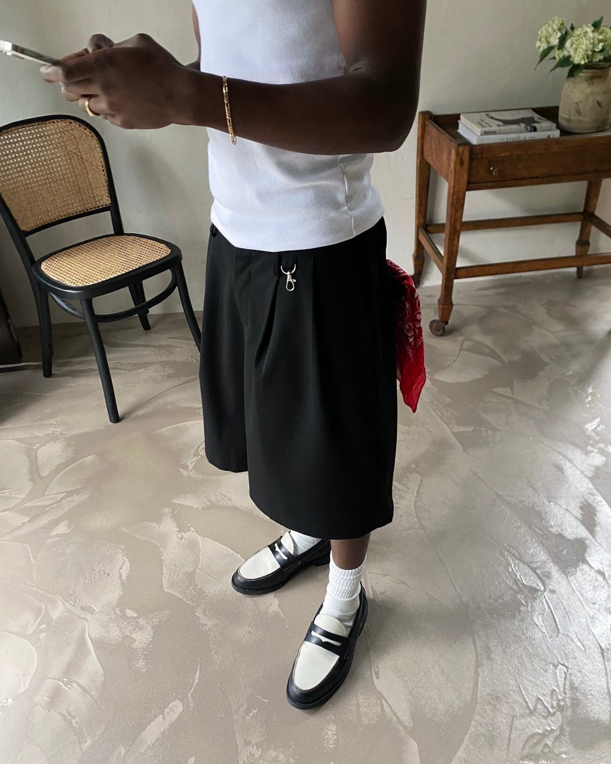 Person wearing black pleated tailored shorts, white tank top, and black white loafers.