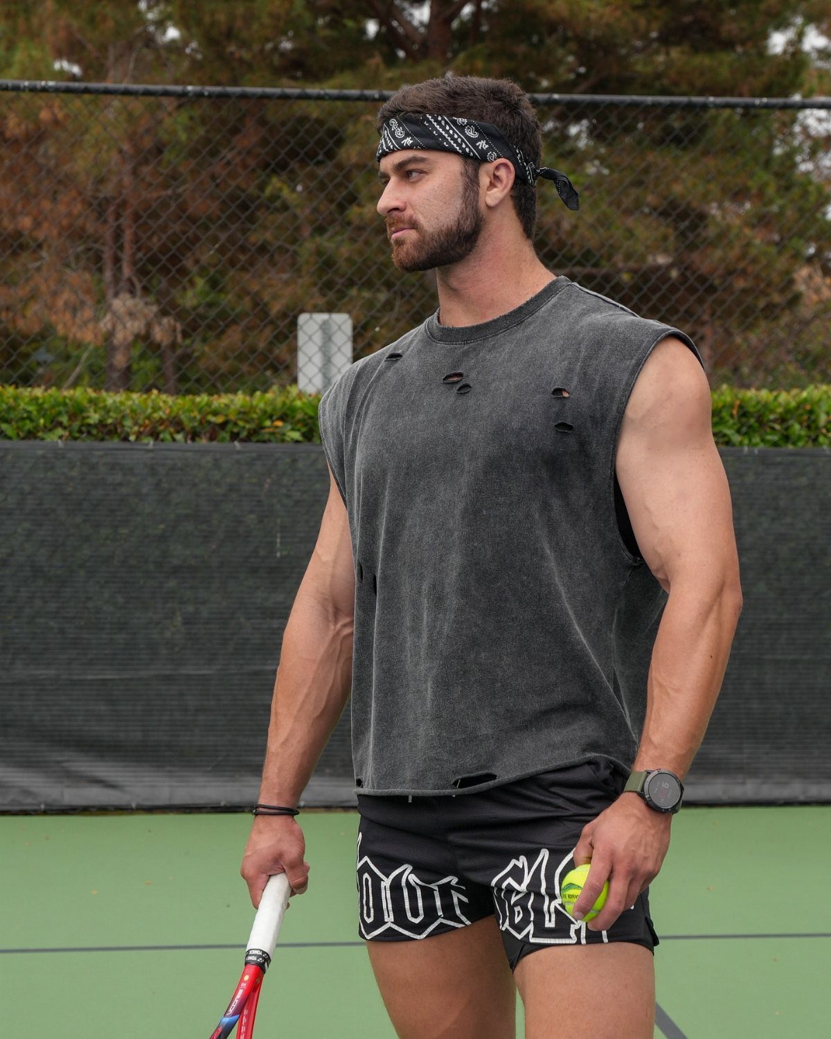 Muscular man in grey sleeveless shirt and black shorts on a tennis court.
