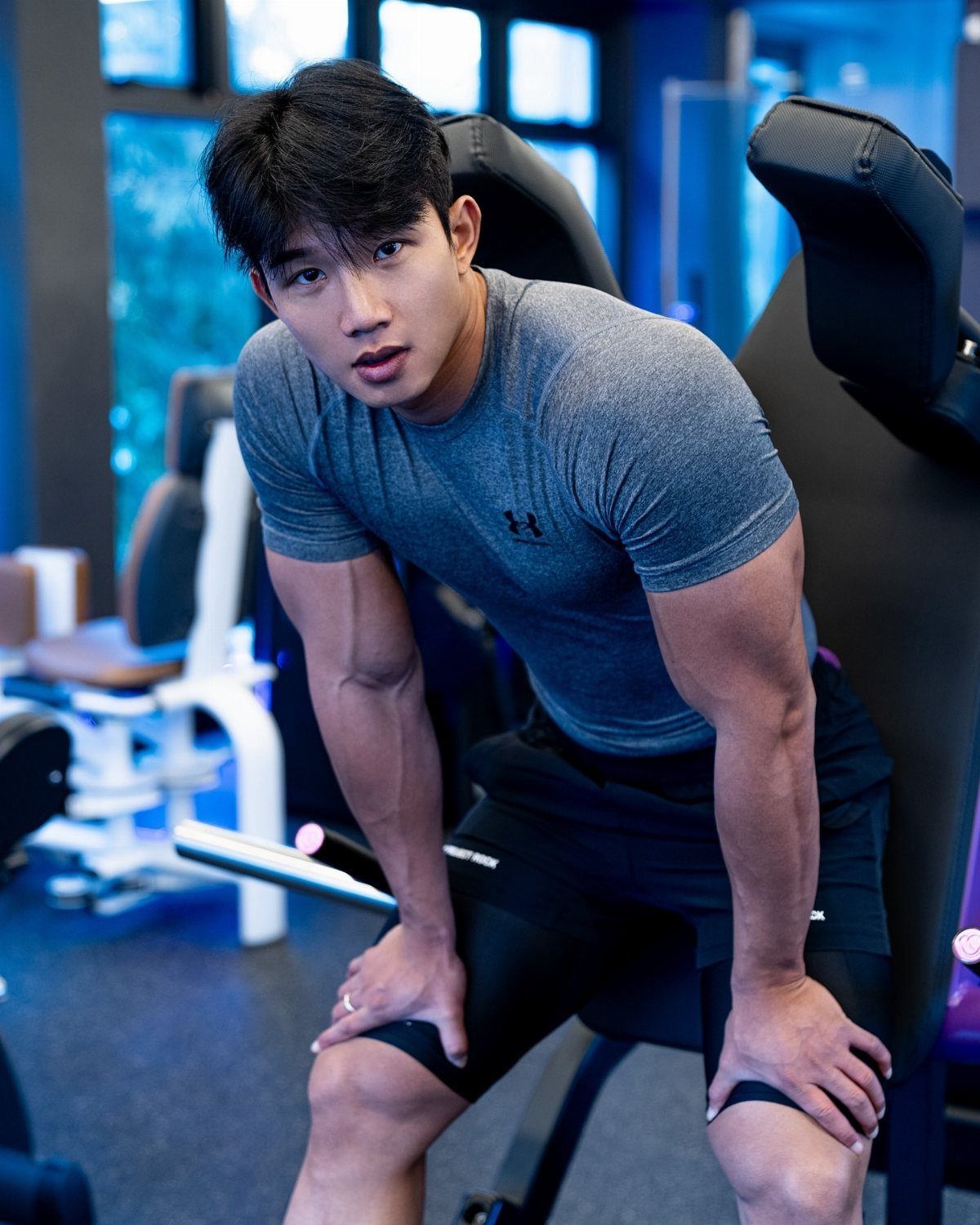 Muscular man wearing a grey short-sleeve compression shirt and black shorts in a gym.