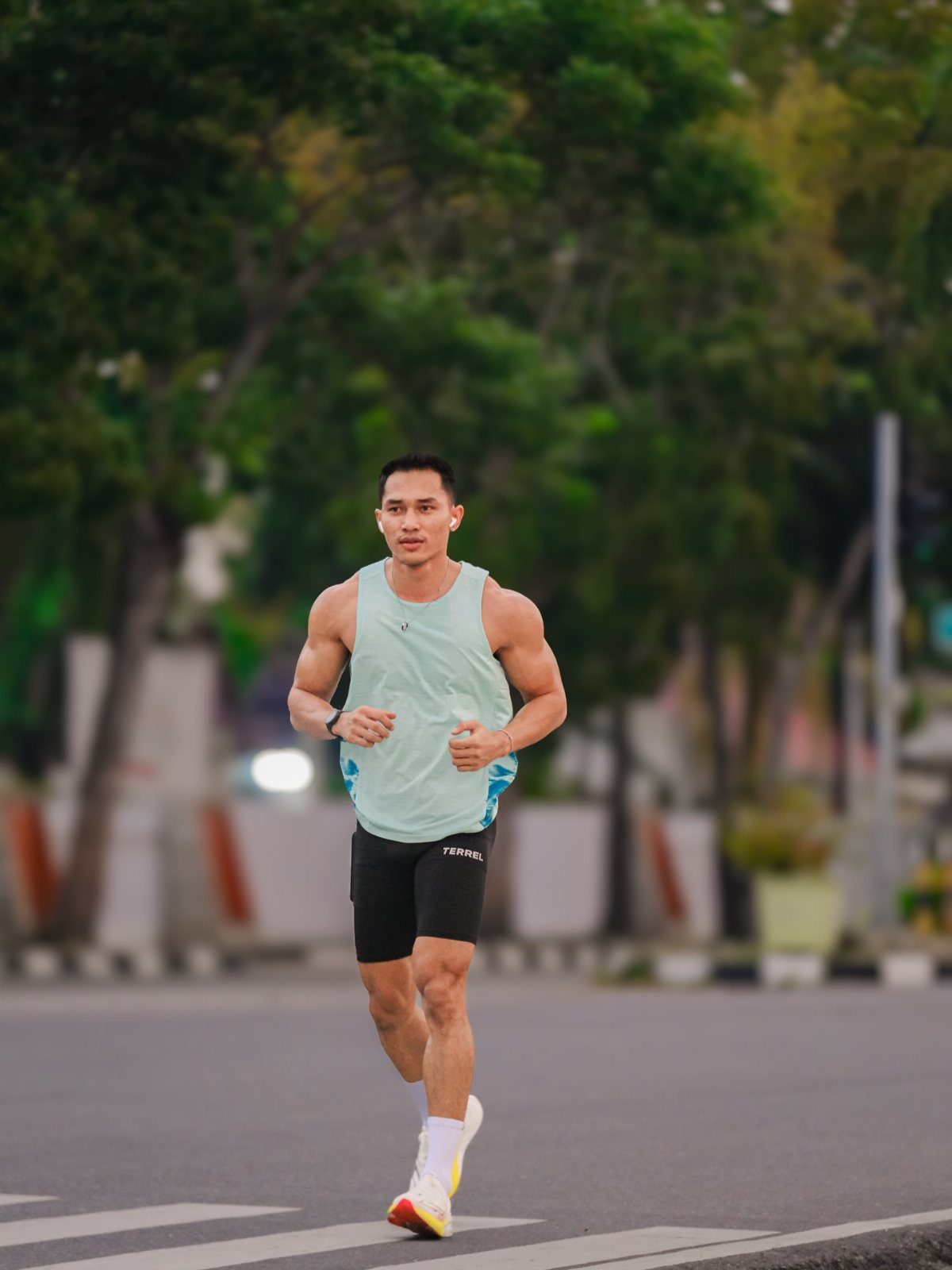 Man running on a city street wearing a light blue tank top and black shorts