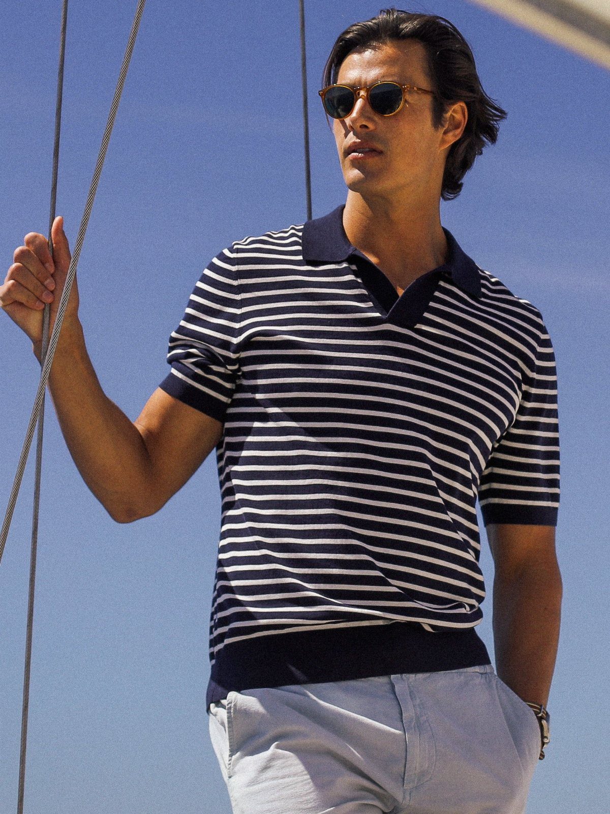 Man in striped polo shirt and light blue chinos on a sailboat