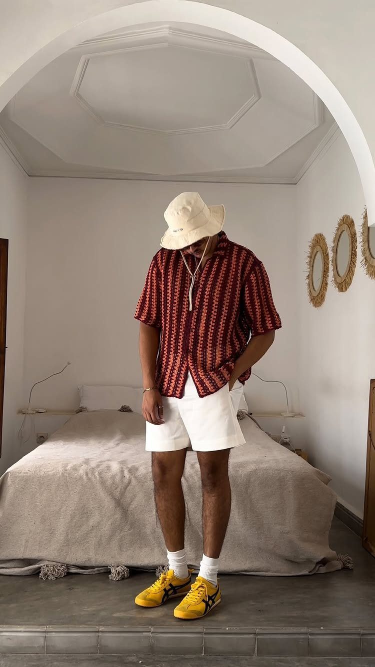 Man wearing a red patterned shirt, white shorts, and yellow sneakers in a room.