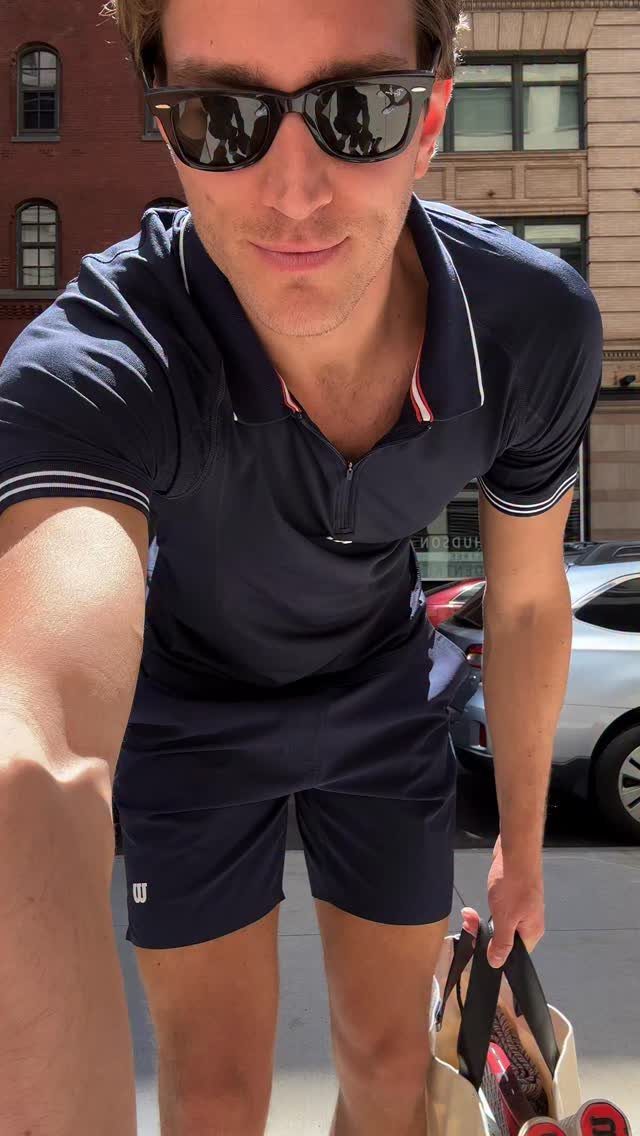 Man in navy blue polo shirt and athletic shorts holding a sports bag.