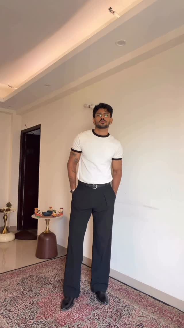 Man wearing a tucked white t-shirt with black trim and black tailored pants.