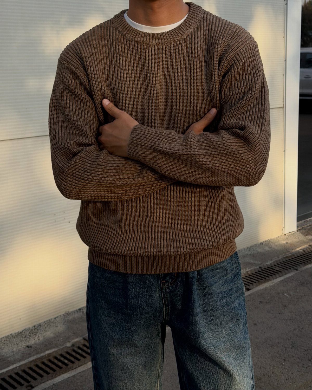Person wearing a brown ribbed knit oversized sweater and blue denim jeans outdoors.