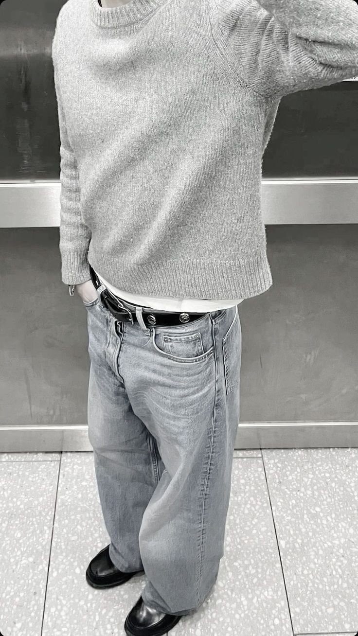 Person wearing a grey crewneck sweater and light-wash grey jeans with black shoes.