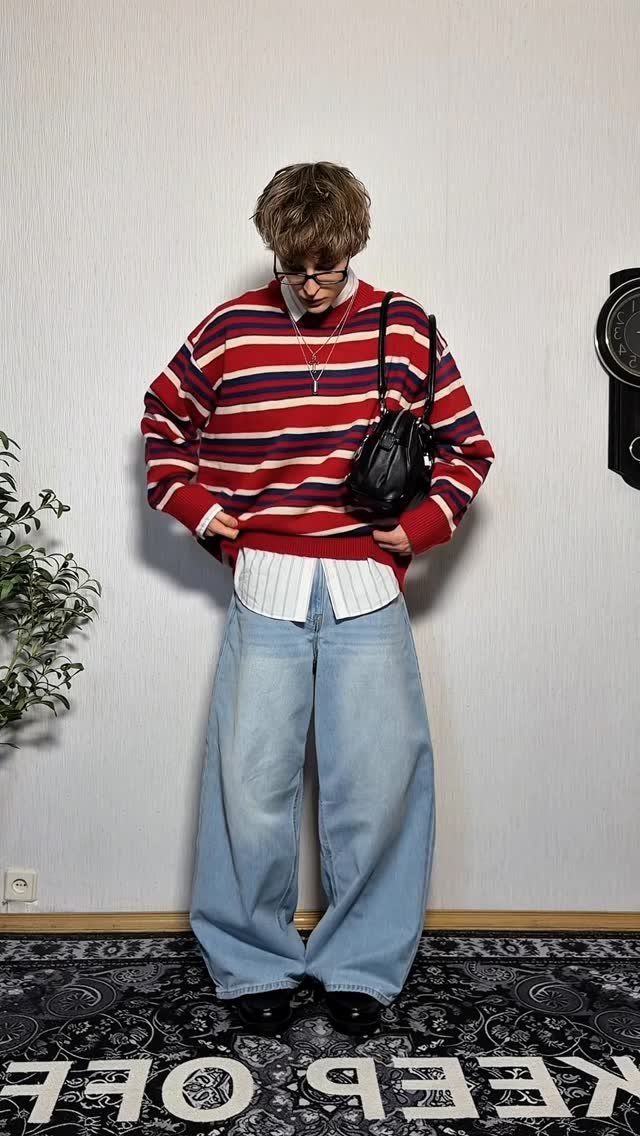 Person wearing a striped red sweater and wide-leg light blue jeans standing indoors.