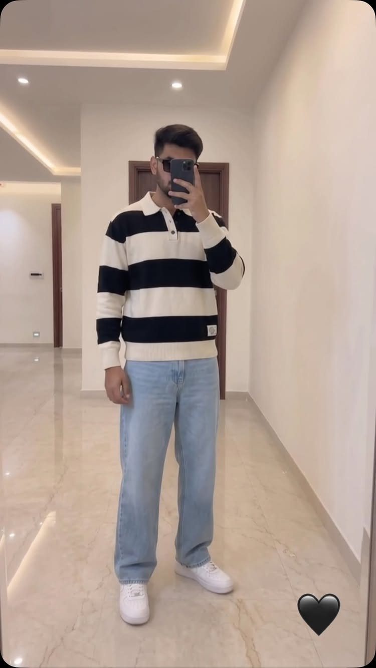 Man wearing a striped polo sweater, light blue wide-leg jeans, and white sneakers.