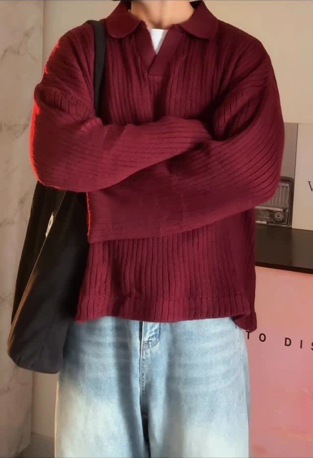Person wearing a burgundy ribbed sweater and light blue jeans with a black bag