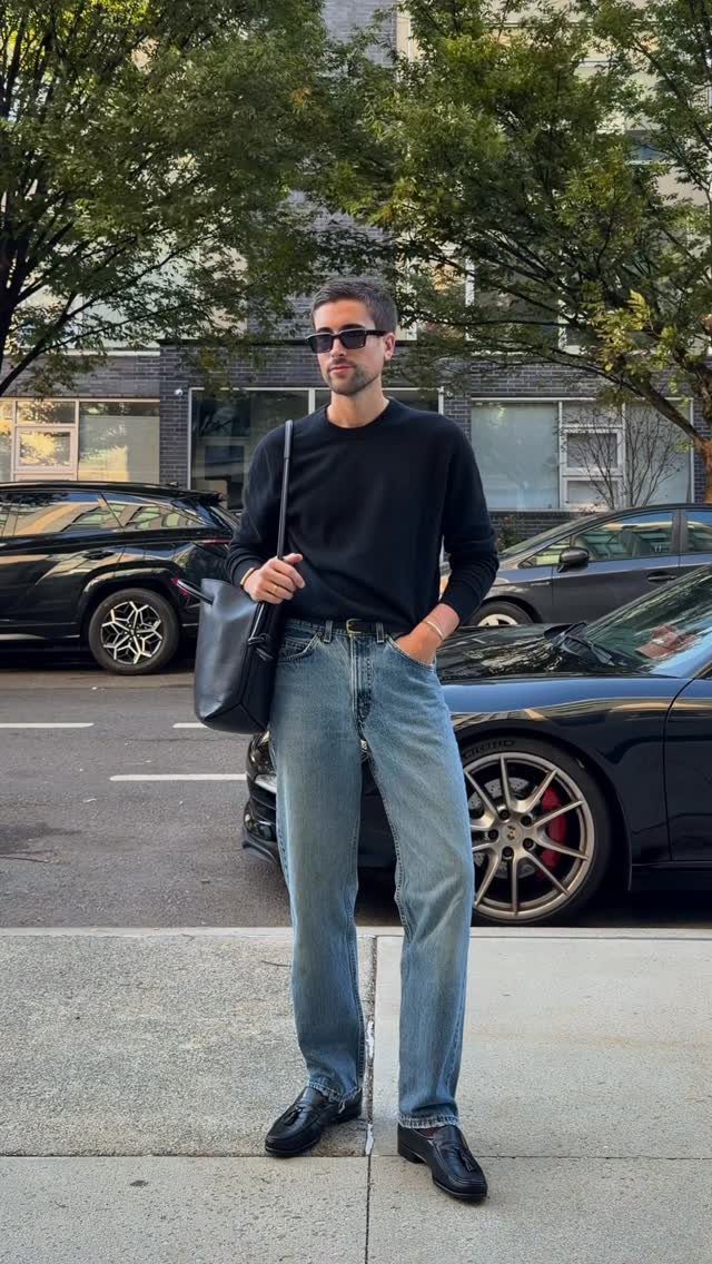Man wearing a black crewneck sweater and light blue jeans on a city street