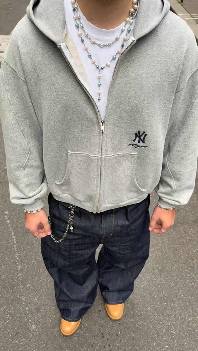 Person wearing grey zip-up hoodie, white t-shirt, dark wide-leg jeans and beaded necklaces.