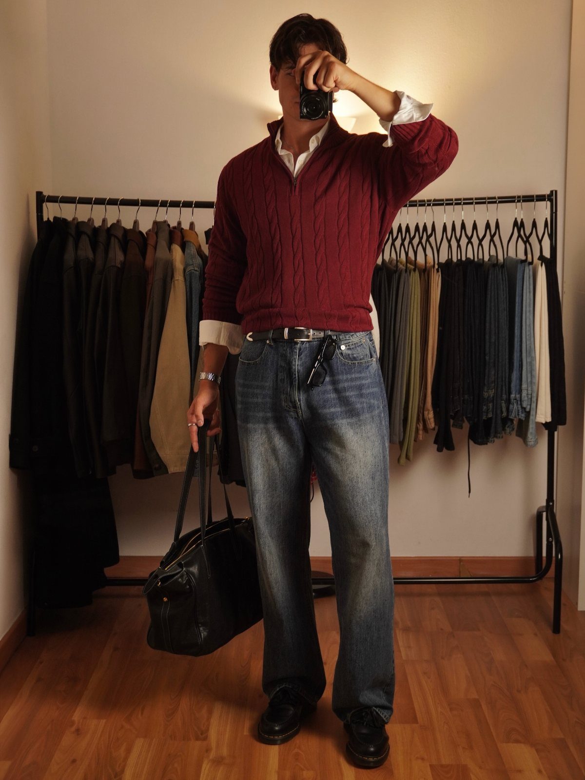Man in red cable-knit sweater and blue jeans layering a white collared shirt.