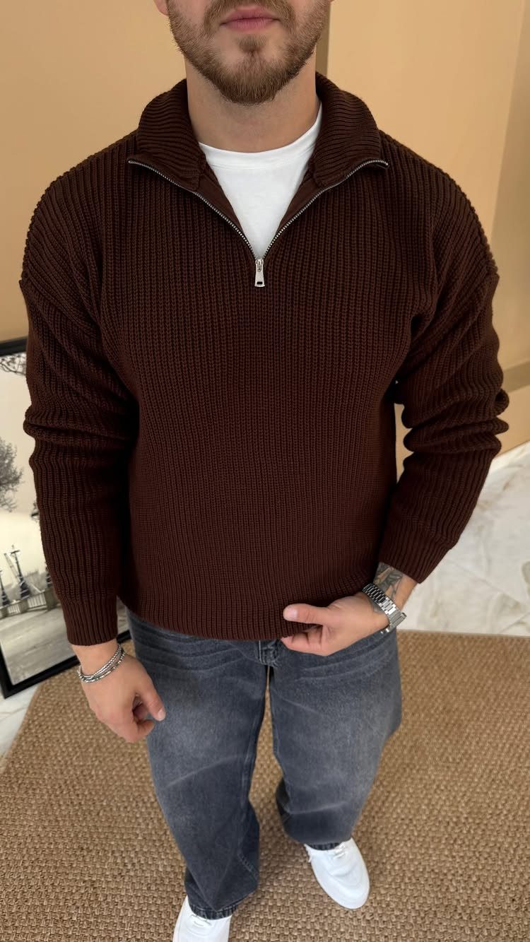 Man wearing a brown quarter-zip ribbed sweater with grey jeans and white sneakers.