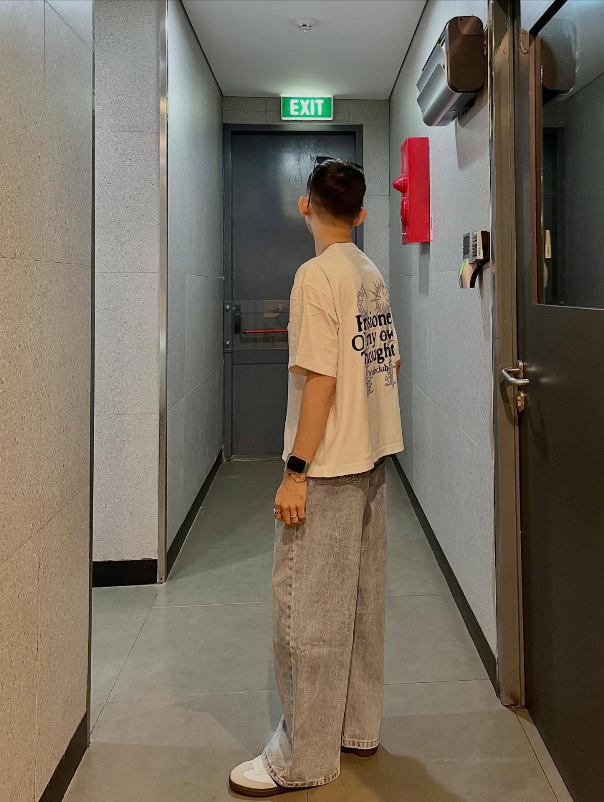 Person wearing an oversized cream t-shirt and wide-leg light grey jeans in a hallway