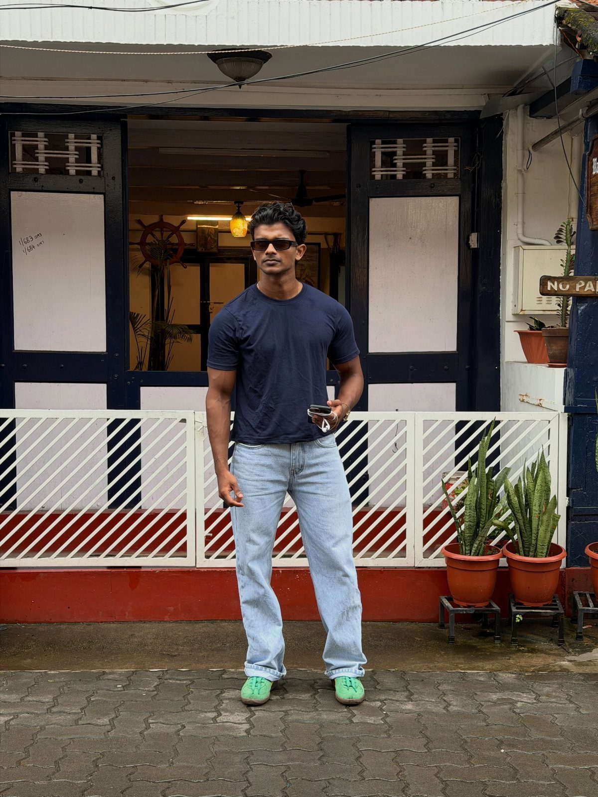 Man wearing a dark blue t-shirt and light blue jeans standing outdoors.