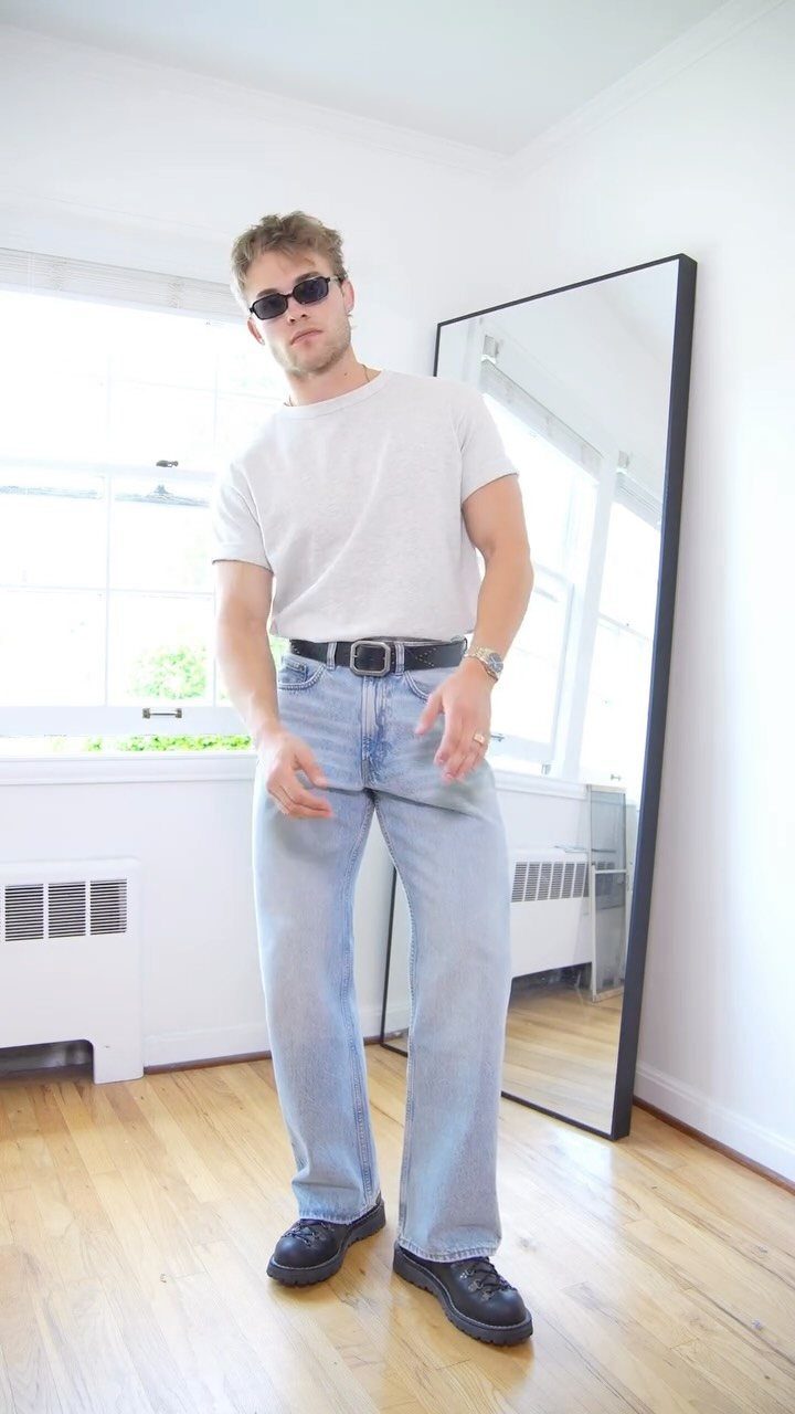 Man in white t-shirt and light blue jeans posing in a bright room.